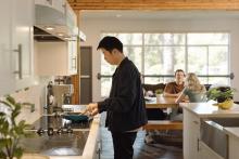 Student preparing food in a Robson Hall kitchen while others sit at a dining table.