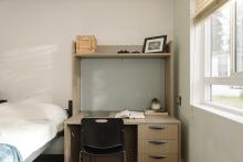 Study desk and chair beside a bed and window in a residence room.