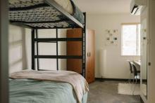 Furnished residence room with a bunk bed, desk, chair and window.