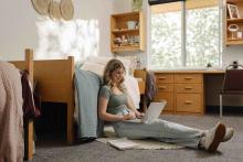 Student using a laptop while seated on the floor of a Robson Hall residence room.