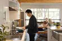 Student preparing food in a Robson Hall kitchen while others sit at a dining table.