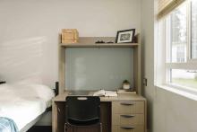 Study desk and chair beside a bed and window in a residence room.