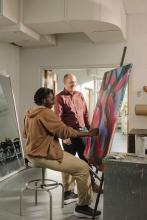 Student painting on a large canvas while an instructor observes in an art studio.