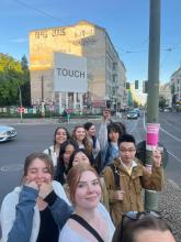 Group of students taking a selfie on a city street beside a graffiti-covered building and public artwork.