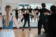 Group fitness instructor leading participants through a movement exercise in a mirrored studio.