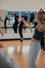 Fitness instructor demonstrating a movement while participants follow along in a studio.
