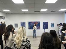 Presenter speaking to a group of visitors in an art gallery surrounded by colourful paintings.