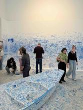 Visitors exploring an immersive installation covered in blue handwritten notes, drawings, and markings.
