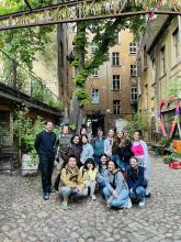 Group of students posing together in a leafy courtyard surrounded by historic buildings.