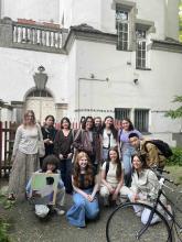Group of students posing outside a building, with one student holding a painting and a bicycle in the foreground.