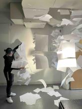 Student arranging a suspended installation made of white paper in an art studio.