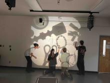 Students creating drawings with projected light and shadows on an art studio wall.