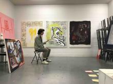 Student seated in an art studio surrounded by large abstract paintings.