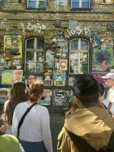 Students viewing a brick wall covered with street art, posters, and graffiti.