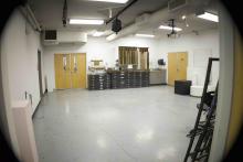 Wide view of an art studio with open workspace, easels, storage cabinets, and a ceiling-mounted projector.