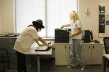Two students using a paper cutter and printer in a SAMC workspace.