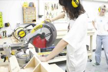 Student wearing hearing protection positions wood at a mitre saw in the SAMC woodworking shop.