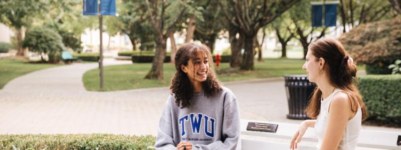 Two female students sitting on a bench talking at the TWU Langley campus.