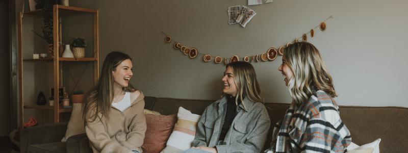 Three female students sitting on a couch in their dorm apartment.