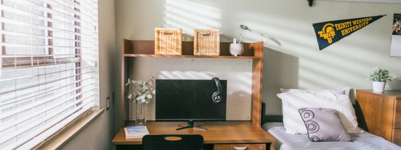 A dorm room with a desk, bed, and wall decorations. 