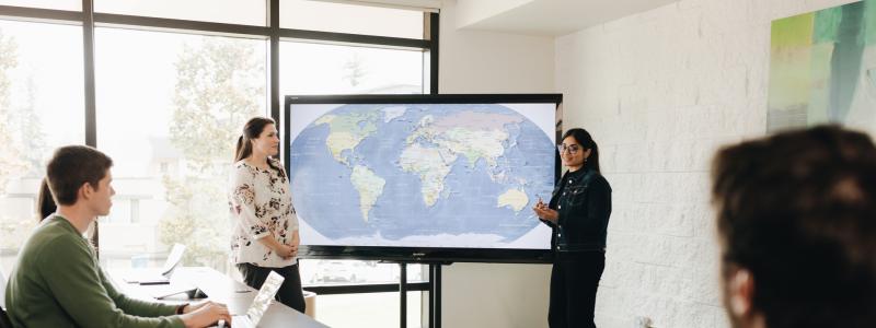 students in a classroom with a professor explaining a map on display