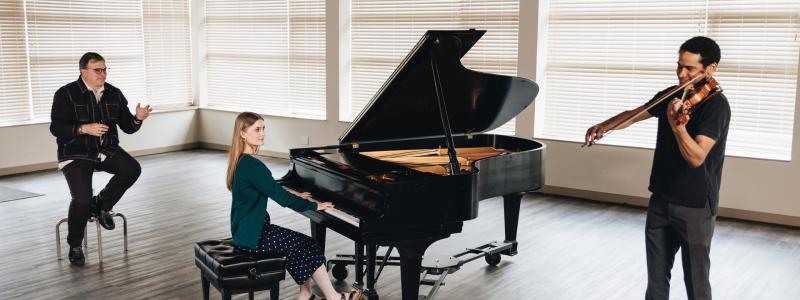 two music students playing the piano and violin for their professor