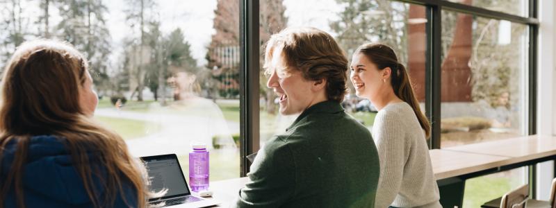 three students seated facing the window and enjoying a discussion