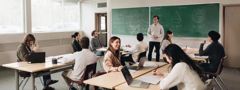 students in science classroom with professor teaching at blackboard