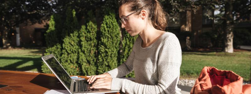 woman using laptop outdoors on wooden table