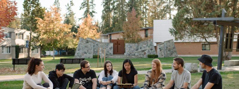 students sitting outside infront of Hanson Garden Chapel reading a bible