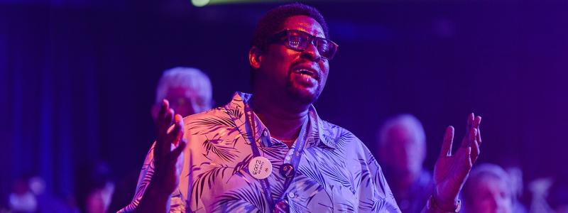 man singing with hands raised in a dark room with colourful lights