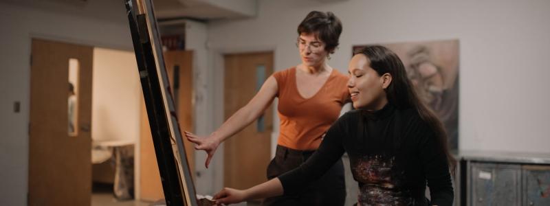 teacher working with students in art studio on painting