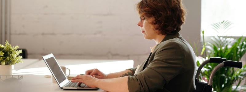 women in a wheelchair sitting at desk and working on a laptop