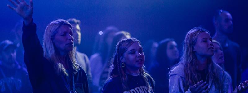 Three people worshiping in chapel in a dimly lit room