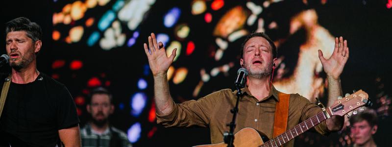 Worship leader with a guitar holding his hands up in praise