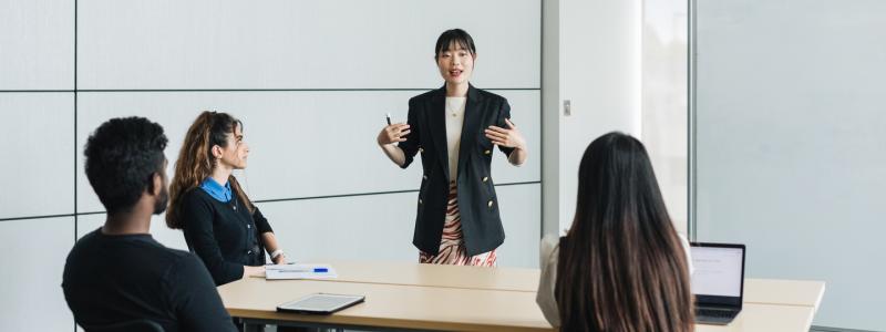 Professionally dressed instructor teaching three students in a white room