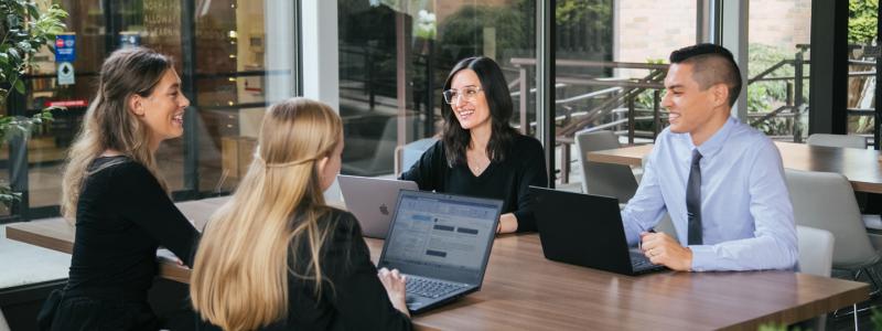 Four people sitting at a desk working or talking