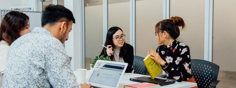 Four people sitting at a desk working or talking