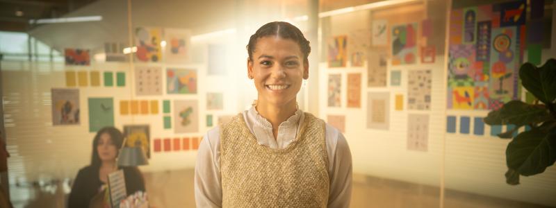 Aliya standing in a room of paintings smiling at the camera
