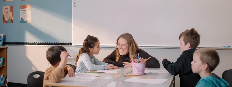 teacher leaning down on desk to work with students