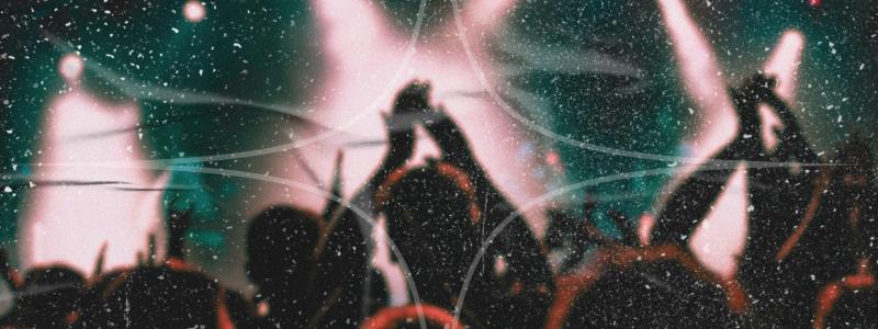 Silhouetted concert crowd with raised hands against bright stage lights, overlaid with a textured grain effect.