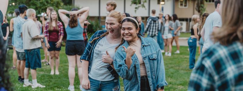 A group of people gathered on a grassy area outdoors. Two young women pose for a photo.