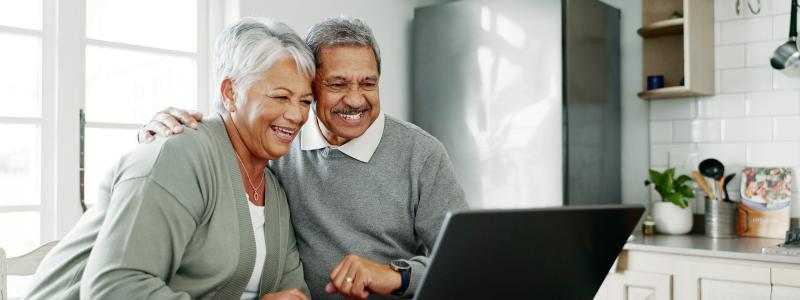 Elderly couple smiling and viewing laptop together at a table
