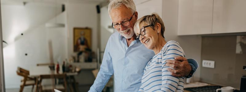Elderly couple smiling and using laptop at kitchen counter