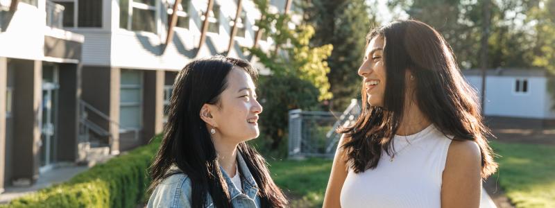 Two women smiling at each other outdoors near a modern building.