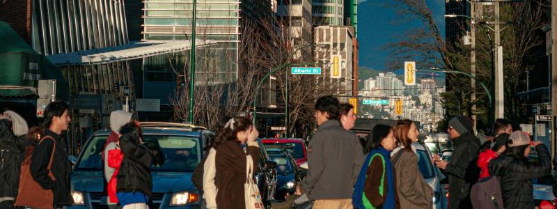 People crossing a busy city street, surrounded by tall buildings and cars.