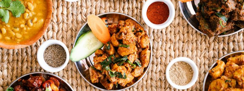 Assorted dishes on woven mat with small bowls of spices.