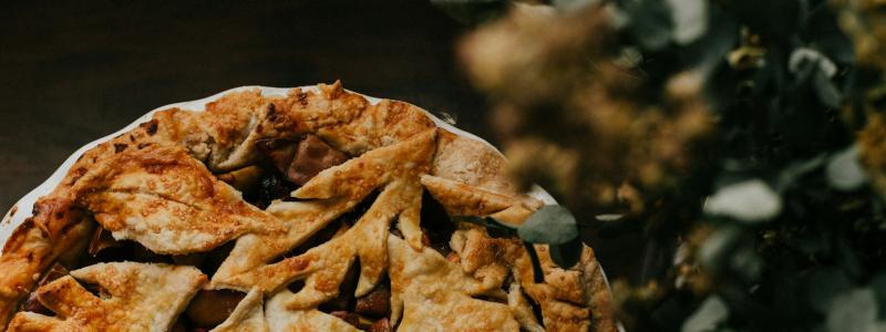 Golden-brown pie with leaf-shaped crust, beside blurred greenery.