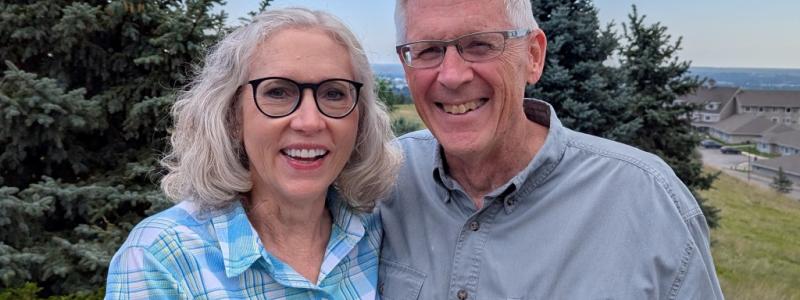 Smiling couple outdoors with trees and clear sky.