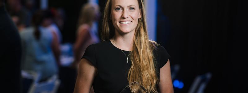 Smiling woman holding an award, standing in a dimly lit room.
